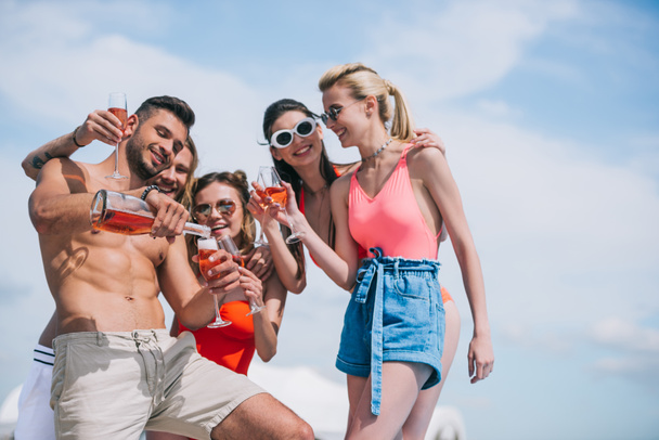 Blick auf glückliche junge Freunde, die an Sommertagen Gläser halten und Wein einschenken - Foto, Bild