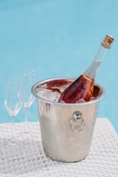 close-up view of bottle of champagne in bucket with ice and two empty glasses at poolside - Fotografie, Obrázek
