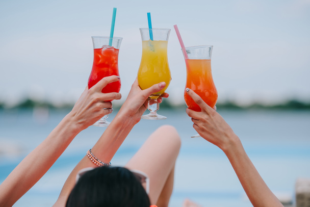 cropped shot of young female friends holding glasses with summer cocktails at beach - Zdjęcie, obraz
