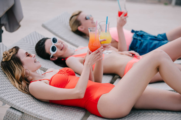 красиві дівчата в купальниках і сонцезахисних окулярах відпочивають з коктейлями на шезлонгах
 - Фото, зображення