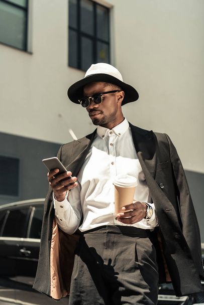 Przystojny młody biznesmen african american, słuchanie muzyki i trzymając kubek kawy - Zdjęcie, obraz
