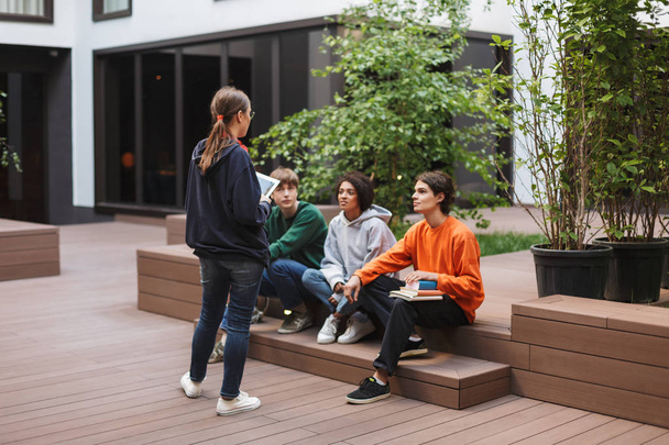 Grupo de estudiantes guays sentados y preparándose para la lección mientras estudian juntos en el patio de la universidad
 - Foto, imagen
