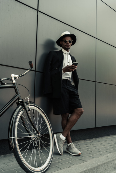 Stylish man wearing white shirt and jacket using smartphone while standing by his bicycle - Foto, Imagem
