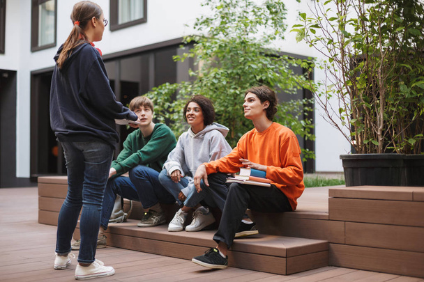 Grupo de jóvenes estudiantes sentados y preparándose para la lección mientras estudian juntos en el patio de la universidad
 - Foto, imagen