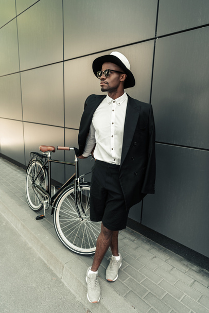 Fashionable african american man wearing fedora hat standing by his bicycle - Foto, Bild