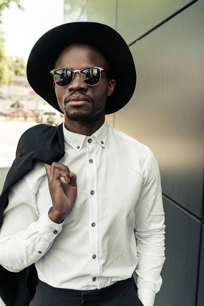 Handsome young african american businessman in sunglasses holding his jacket - Foto, Bild