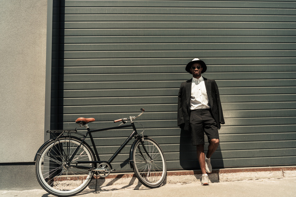 Stylish man wearing white shirt and jacket posing by his bike - Foto, Imagen