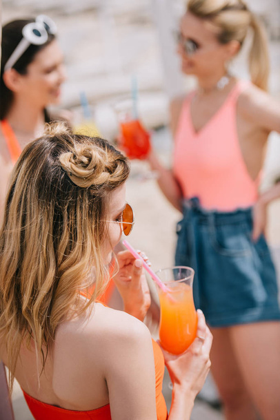 jovem mulher bebendo coquetel de verão enquanto passa tempo com namoradas na praia
 - Foto, Imagem