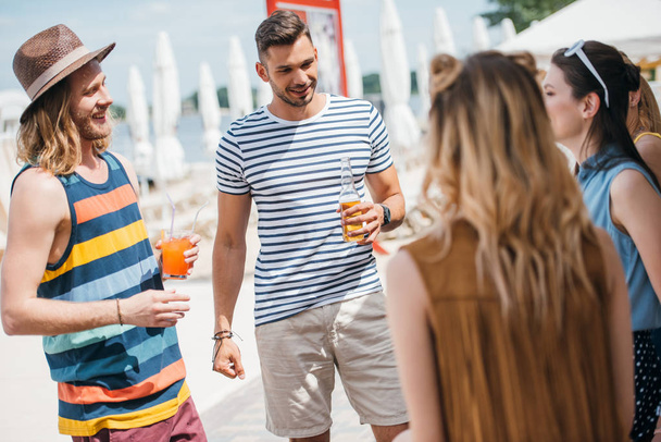 щасливі молоді люди п'ють напої і дивляться один на одного на пляжі
 - Фото, зображення