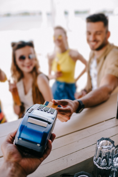 enfoque selectivo del joven que paga con tarjeta de crédito y terminal de pago en el bar de playa
 - Foto, imagen