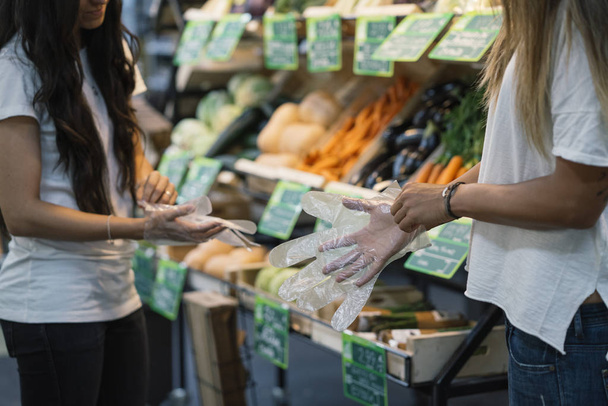 Две женщины, покупающие в супермаркете, надевают перчатки
 - Фото, изображение