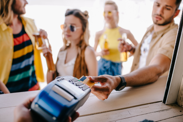 cropped shot of young man paying with credit card and payment terminal at beach bar - Fotó, kép