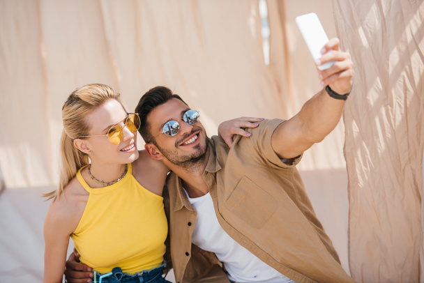 バンガローでスマート フォンで selfie を取ってサングラスの若いカップルの笑顔  - 写真・画像