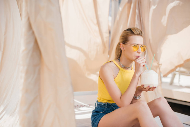 piękna młoda kobieta w okulary orzeźwiający koktajl do picia siedząc w domku - Zdjęcie, obraz