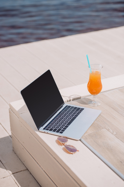 laptop with blank screen, sunglasses and glass with cocktail at beach - Photo, Image