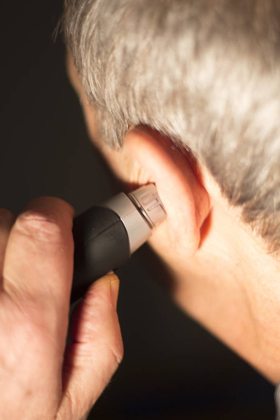 Hombre de la tercera edad cortando el pelo del oído interno con cortador eléctrico
. - Foto, Imagen
