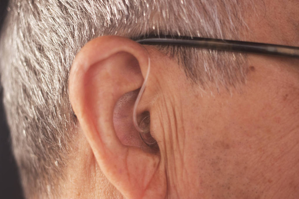 Hombre adulto mayor sordo que usa audífonos digitales modernos de alta tecnología en el oído
. - Foto, imagen