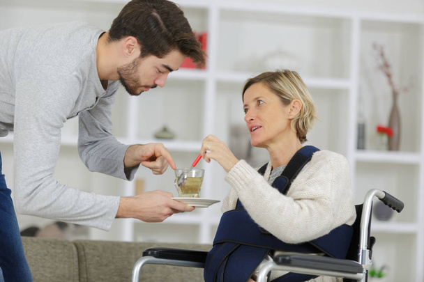 cuidador dando taza de té a la mujer discapacitada en silla de ruedas
 - Foto, imagen