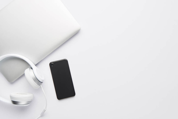 Minimal work space concept. Top view of laptop, white headphones and black cell phone on white background with copy space. Flat lay. - Foto, afbeelding