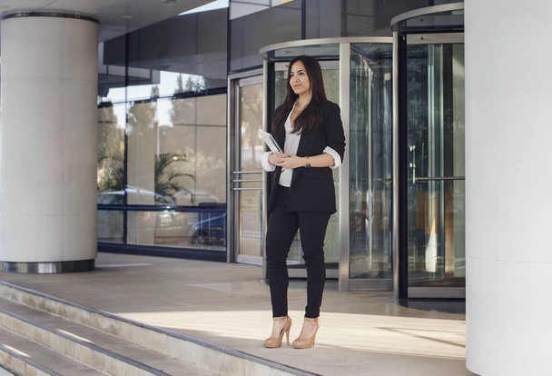 Young hicpanic business woman stading at the doors of her office holding papers - 写真・画像