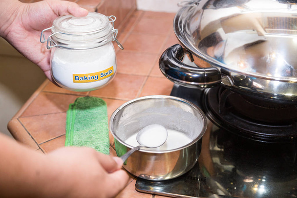 Henkilö, jolla on lusikallinen sekoitettua ruokasoodaa, tehokas luonnollinen puhdistusaine kotitalouksien keittiössä
 - Valokuva, kuva