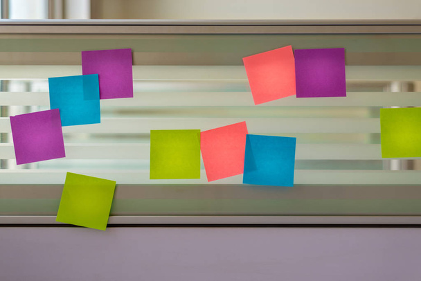 Notas adhesivas de color dispersas aleatoriamente sobre la pantalla de vidrio de un escritorio de banco
 - Foto, Imagen