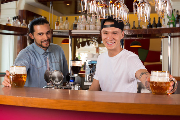 Dois jovens bartenders alegres e felizes que oferecem cerveja aos clientes
. - Foto, Imagem