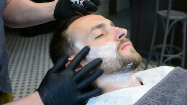 Barbeiro corta barba de clientes com um aparador de barba profissional em uma barbearia em fundo leve, close-up
. - Filmagem, Vídeo