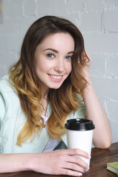 Close-up portrait of a beautiful young girl sitting at a table with coffee and smiling, looking at the camera. Vertical photo - 写真・画像