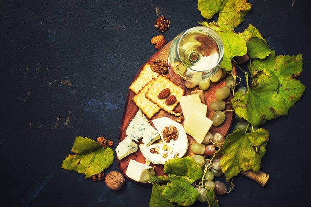 Witte droge wijn, kaas met noten, schimmel, druif en Cracker, donkere achtergrond, bovenaanzicht - Foto, afbeelding