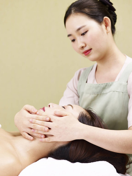 jovem asiático massagista realizando massagem facial na mulher no spa salão
 - Foto, Imagem
