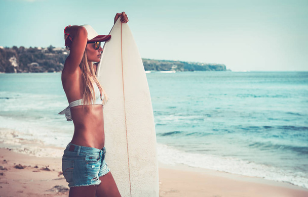 Sportive woman with surfboard on beautiful sandy coast, active hobby, waiting for a good waves, enjoying summer vacation on the beac - Photo, image