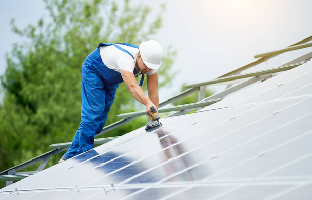 Construction worker connects photo voltaic panel to solar system using screwdriver. Professional installing and construction of solar system, alternative energy and financial investment concept. - Photo, Image