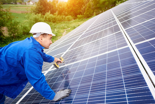 Construction worker connects photo voltaic panel to solar system using screwdriver. Professional installing and construction of solar system, alternative energy and financial investment concept. - Foto, imagen