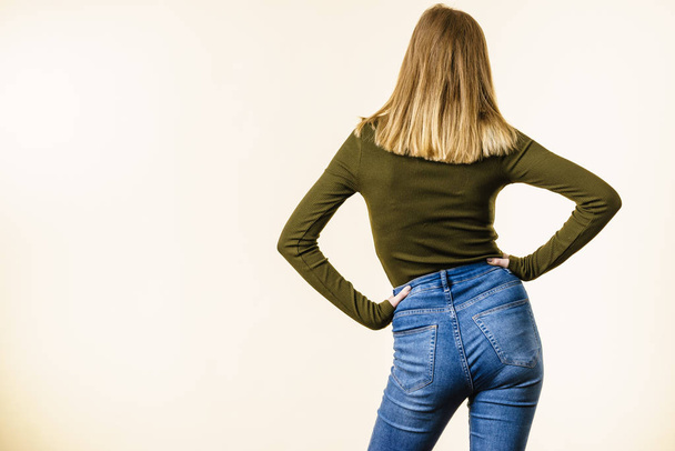 Unrecognizable woman standing backwards wearing slim fit blue jeans and khaki top, white background with copy space. - Photo, Image
