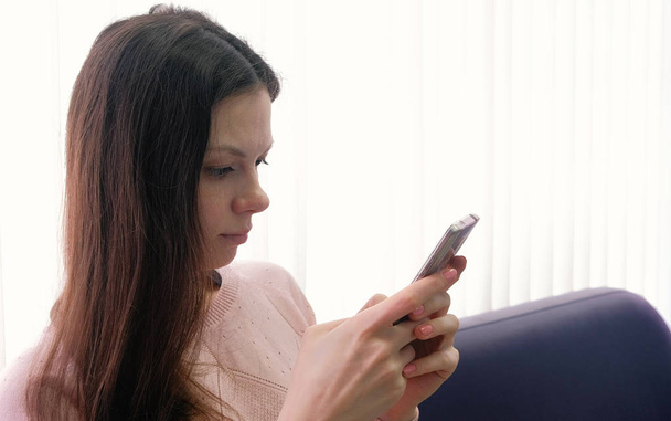 Young woman brunette is typing a message on her mobile phone and looking at screen. Side view - Photo, Image