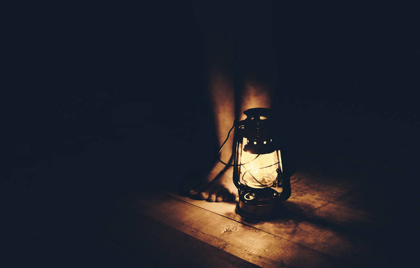 Girl legs on a wooden floor under the light from a oil lamp in the dark. - Фото, зображення