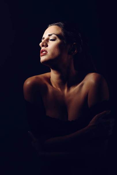 Młoda brunetka Kobieta w czarnej bieliźnie w chiaroscuro oświetlenia. Atrakcyjna dziewczyna, model mody. Strzał studio. - Zdjęcie, obraz