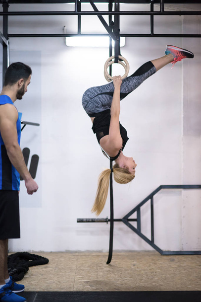 young athletic woman working out with personal trainer on gymnastic rings at the cross fitness gym - Foto, afbeelding
