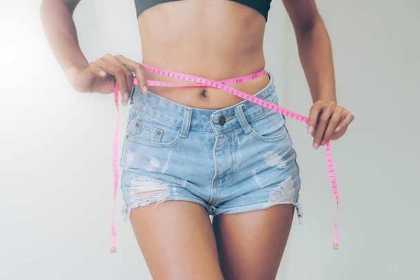 Молодая стройная женщина измеряет свою талию, измеряя ленту за диетой на белом фоне. Концепция успеха потери веса
. - Фото, изображение
