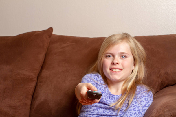 Девушка держит дистанционно, пока она смотрит телевизор
 - Фото, изображение
