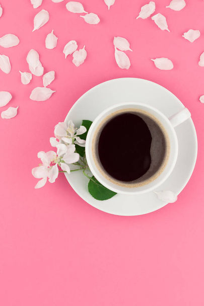 Δημιουργική επίπεδης lay έννοια κάτοψη του φλιτζάνι καφέ και λευκό δέντρο της apple λουλούδια πέταλα σε παστέλ ροζ φόντο με αντίγραφο χώρος σε minimal στυλ, πρότυπο για το κείμενο - Φωτογραφία, εικόνα