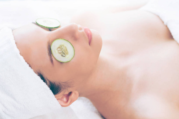Relaxed young woman getting eye nature treatment by cucumber at luxury spa resort. Wellness and healing concept. - Photo, Image