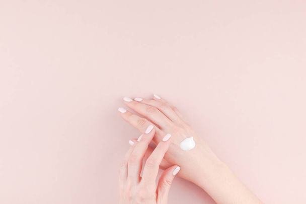 Creative image of woman moisturizing her hand with cosmetic cream lotion with copy space on millennial pink background in minimalism style. Concept template feminine blog, social media, beauty concept - Fotografie, Obrázek