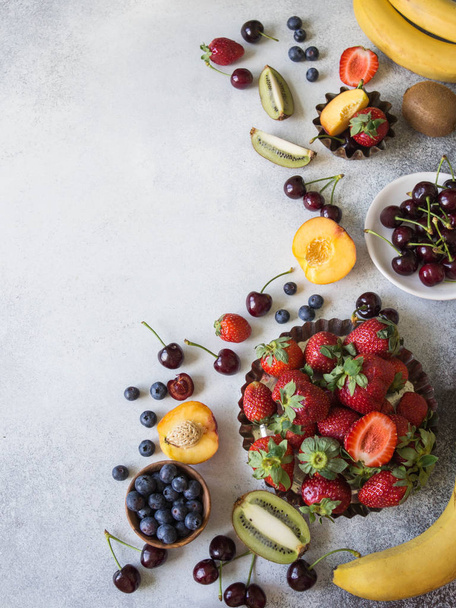Erilaisia marjoja ja hedelmiä harmaalla taustalla. Mansikat, kirsikat, kiivi, persikka, mustikat ja banaanit Top view
 - Valokuva, kuva