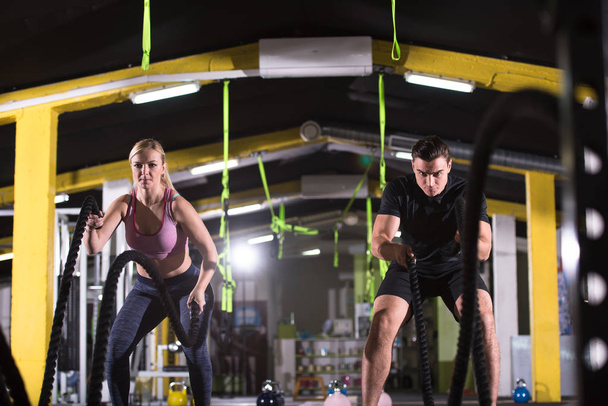 young fit sports couple working out in functional training gym doing  battle ropes cross fitness exercise - Fotografie, Obrázek