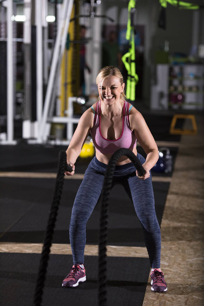 young fit athlete woman working out in functional training gym doing  battle ropes exercise as part of cross fitness training - Foto, Bild