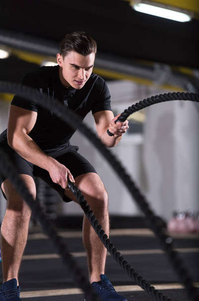 young fit athlete man working out in functional training gym doing  battle ropes exercise as part of cross fitness training - Фото, зображення