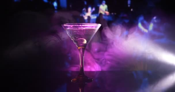 sklenice s martini s olivou uvnitř. Zblízka pohled na sklo s klubovým nápojem na tmavém mlhavém tónovaném pozadí. Selektivní soustředění. Koncept klubového pití - Záběry, video