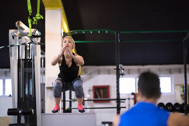 young athletic woman training with personal trainer  jumping on fit box at cross fitness gym - Foto, Imagen